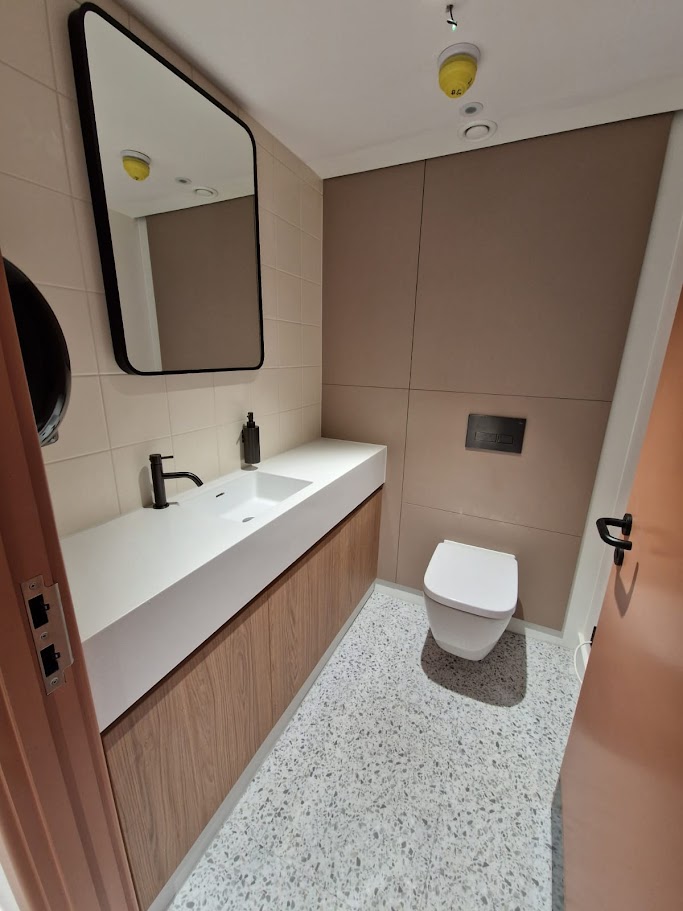 Solid surface vanity basin and woodgrain vanity unit beside a wall-hung WC