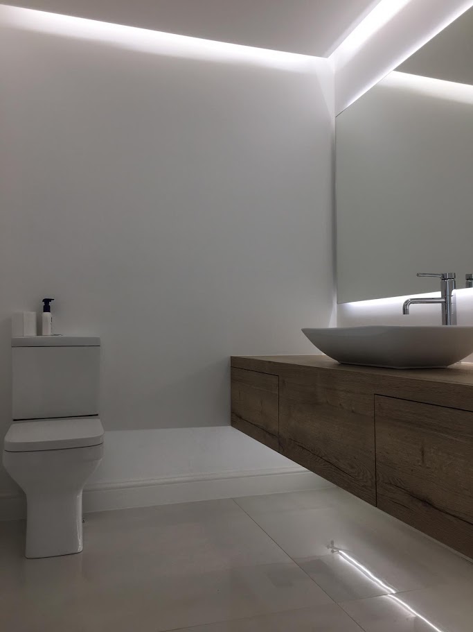 A floating woodgrain vanity unit with a vessel basin under a back-lit mirror
